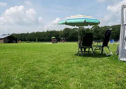 Ruim grasveld met kampeerplaats, parasol en speeltuin op Bospark Aagjeshoeve in Schoonoord op de Hondsrug, Drenthe