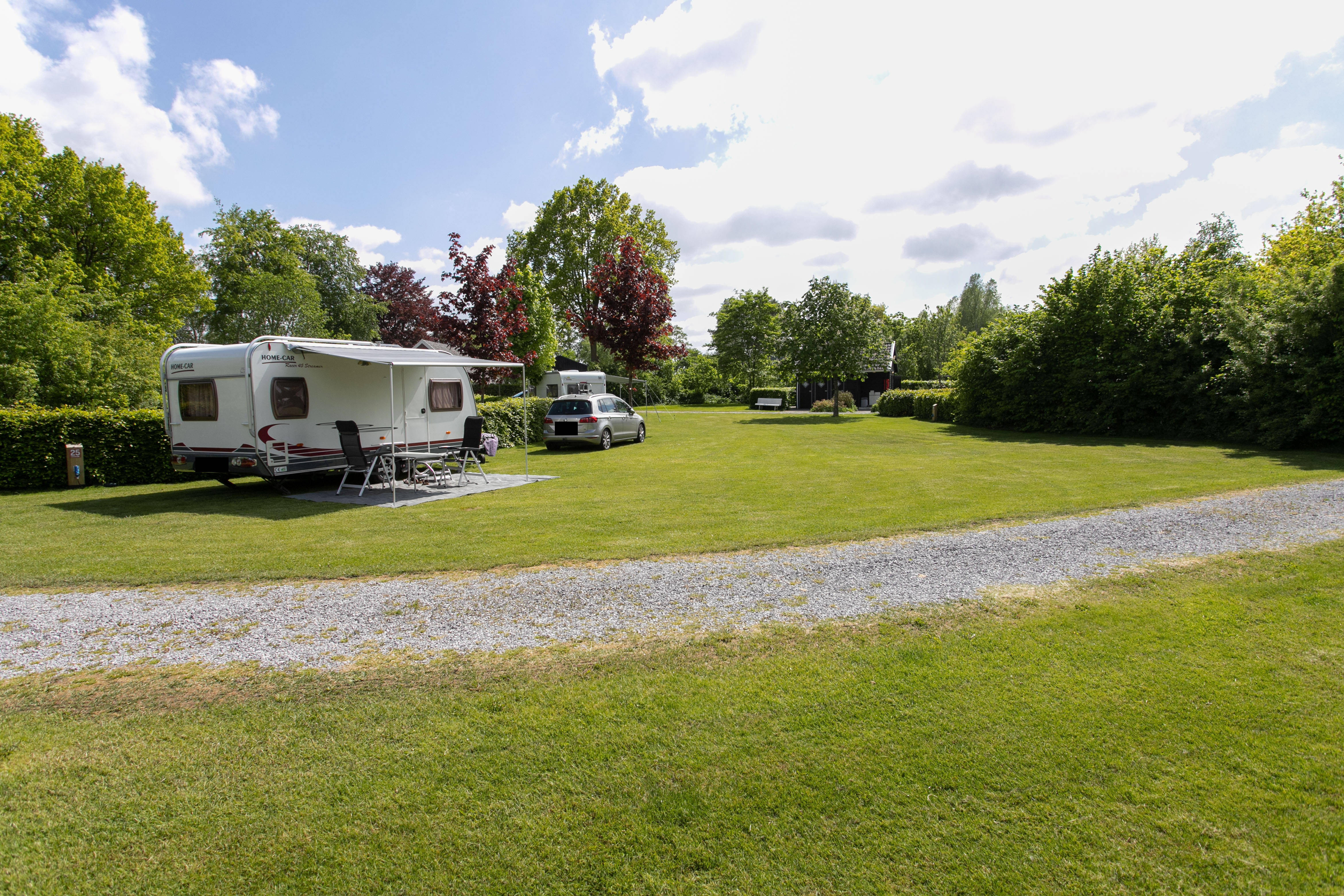 Elektrische auto naast een caravan op een ruime kampeerplaats bij Camping de Oosterweide in Pesse, Drenthe